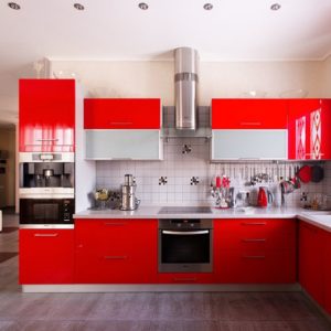 Красная современная угловая глянцевая кухня с высокой духовкой и столешницей вдоль окна